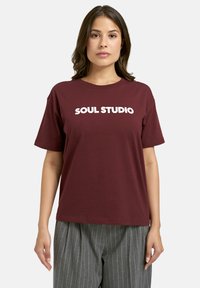 Maroon cotton t-shirt with short sleeves and a round neck, featuring bold white text "SOUL STUDIO" on the front. Casual fit.