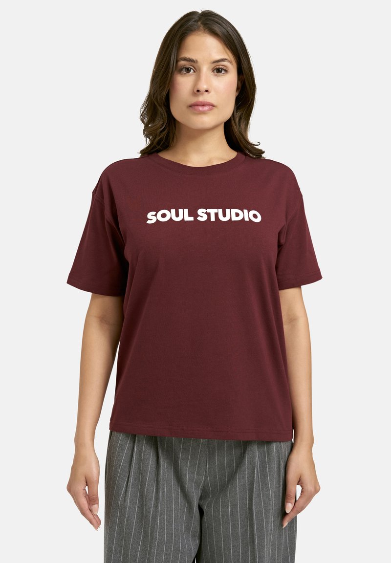 Maroon cotton t-shirt with short sleeves and a round neck, featuring bold white text "SOUL STUDIO" on the front. Casual fit.