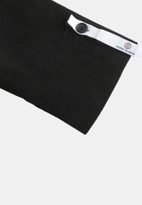 Tissu noir, texturé, comportant une fermeture à bouton avec une étiquette blanche marquée "Serge Blanco". Le design est simple et rectangulaire.