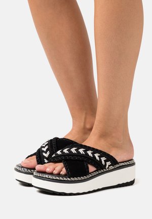 Black wedge sandals with cross straps featuring white embroidery. Cushioned sole, textured upper, and a contrasting white platform.