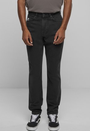 Fekete farmernadrág egyenes szárú szabással, ötlukú kialakítással és megerősített varrással, fekete-fehér tornacipővel párosítva.