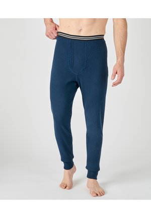Uomo che indossa leggings termici blu navy con fascia elastica a righe, in piedi a piedi nudi su uno sfondo chiaro e semplice.