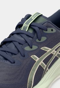 Tengerészkék ASICS futócipő texturált szövettel, vastag tengerészkék fűzőkkel, menta zöld márkajelzéssel ellátott nyelvfüllel és csíkos oldallogó mintázattal.