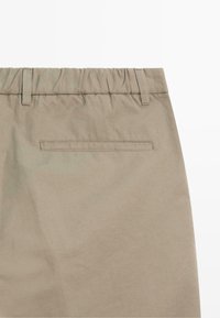 Pantalon en coton beige avec taille élastique, passants pour ceinture et une poche arrière horizontale avec détail cousu.