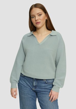 Hellblaues, geripptes Strickoberteil mit V-Ausschnitt und Kragen, langärmelig und in lockerer Passform, kombiniert mit blauen Denim-Jeans.