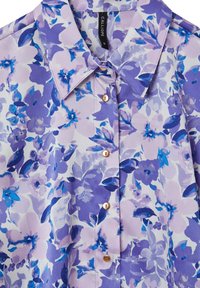 Blouse florale dans des nuances de lavande et de bleu, avec un col, une fermeture à boutons et un tissu léger et lisse avec une finition brillante.