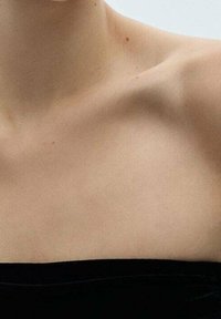 Top negro sin tirantes con un escote de tela suave, que presenta un diseño limpio y sencillo y un ligero brillo. Tonalidad de piel visible en los hombros.