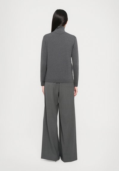 Pull en col roulé gris en tissu doux avec des manches longues, associé à un pantalon gris ample et large en matière texturée.