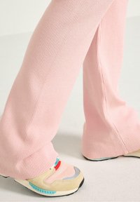 Pantaloni a coste rosa con gamba larga, abbinati a sneakers multicolori realizzate in suede, rete e gomma.