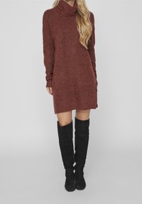 Abito in maglia di colore bordeaux, con colletto alto, maniche lunghe e una silhouette leggermente svasata, abbinato a stivali neri alti fino alla coscia.