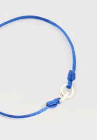 Μπλε πλεκτό βραχιόλι με ασημένιο κούμπωμα και ρυθμιζόμενους κόμπους σε απλό ανοιχτό φόντο.