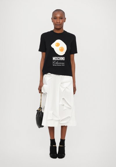 Tricou negru cu mânecă scurtă, cu grafică de ou și textul "MOSCHINO Colazione Primăvară Vară 2025", asortat cu o fustă albă sculptată și pantofi cu toc.