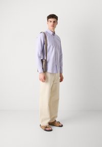 Lichtpaarse overhemdd, crèmekleurige brede broek, en bruine sandalen met verstelbare banden. Eenvoudig ontwerp en een relaxte pasvorm.