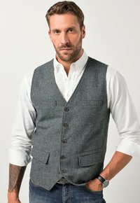 Grauer Tweed-Weste mit V-Ausschnitt, sechsknöpfiger Front, zwei Fronttaschen, getragen über einem weißen Hemd. Sie zeichnet sich durch einen klassischen Schnitt und einen strukturierten Stoff aus.