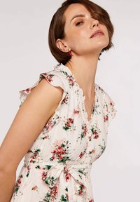 Floral dress featuring a white fabric with pink and green patterns, ruffled sleeves, a V-neck, and a waist tie. Buttons along the front.