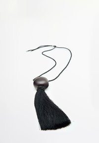 Collana con nappina nera e una sfera in legno, caratterizzata da una corda intrecciata e nappine morbide e fluenti. Design semplice e minimalista.