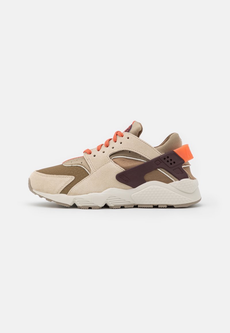 Baskets beige et marron avec lacets orange et languette au talon, semelle blanche épaisse et sangle de soutien marron foncé autour du talon.