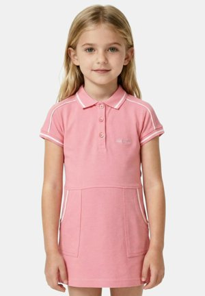 Jeune fille aux longs cheveux blonds portant une robe polo rose à manches courtes avec un liseré blanc et des poches à l'avant, se tenant devant un fond blanc.