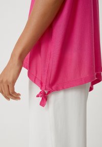 Top leggero di un brillante colore rosa, con una vestibilità ampia, caratterizzato da legami laterali annodati e un tessuto testurizzato, abbinato a pantaloni di tessuto bianchi.