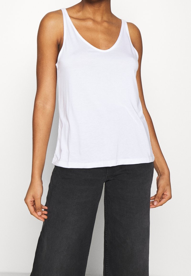 Woman wearing a plain white sleeveless top and high-waisted black wide-leg pants, shown from neck to mid-thigh against white background.