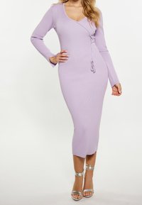 Robe midi en maille côtelée lavande avec manches longues, décolleté en V, design croisé et lien ajustable. Talons argentés à lanières complètent la tenue.