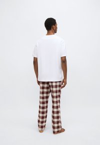 Weißes T-Shirt mit kurzen Ärmeln, kombiniert mit locker sitzenden karierten Schlafanzughosen in Rot und Creme. Das Ensemble besteht aus weichem Stoff mit einem entspannten Schnitt.