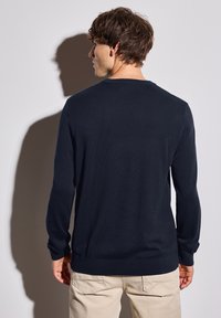 Marineblauer Rundhals-Pullover aus weichem Strickstoff, mit langen Ärmeln und gerippten Bündchen, von hinten gegen einen neutralen Hintergrund gezeigt.