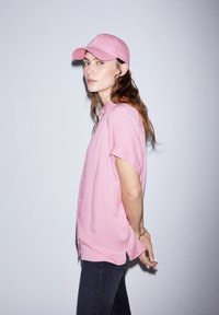 Pink short-sleeve button-up shirt paired with a matching pink baseball cap. The shirt features a smooth texture and side slits.