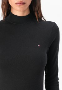 Maglione a collo alto nero realizzato in tessuto liscio, con una vestibilità slim e un piccolo logo ricamato in rosso, bianco e blu sul petto.