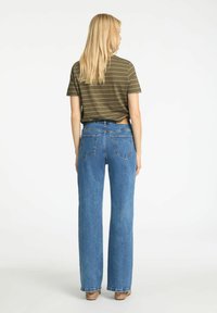 Jeans in denim blu a vita alta con gamba dritta, dotati di tasche posteriori e un'etichetta in pelle, abbinati a una camicia a maniche corte a righe verdi.