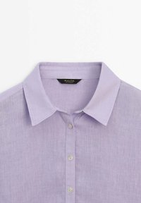 Lavender button-up shirt with a structured collar, plain texture, and small white buttons. Label is black with white text inside the collar.