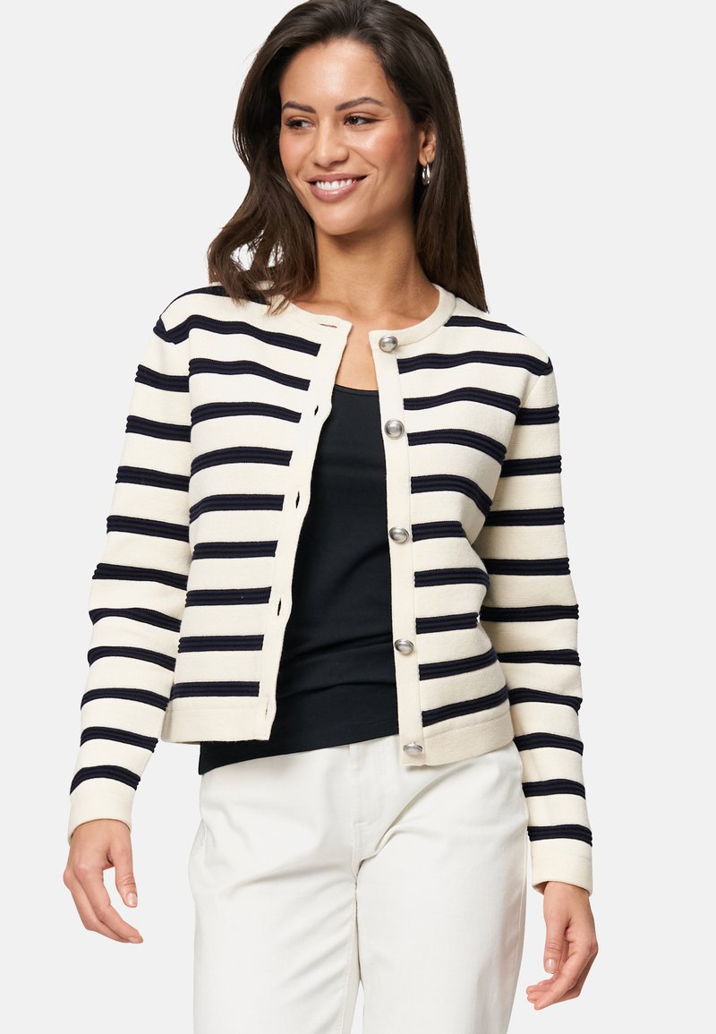 Gilet rayé en crème et marine, avec un col rond, des fermetures à boutons et une texture côtelée le long des rayures. Coupe décontractée.