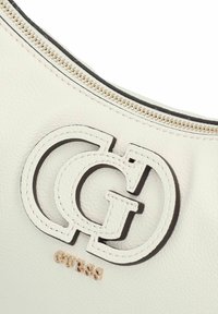 Borsa a tracolla in pelle bianca con un prominente logo interlocking "G" in nero e un accento "GUESS" in tonalità oro, dotata di chiusura con zip nella parte superiore.