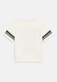 Camiseta blanca de manga corta con dos rayas negras horizontales en cada manga, vista desde la parte de atrás sobre un fondo blanco liso.