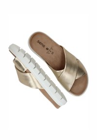 Gouden metallic slide sandalen met een gekruisd ontwerp, een zachte gevoerde voetbed en een witte gestructureerde zool met een verhoogd patroon.