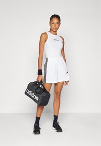 Witte mouwloze top met zwart logo, gecombineerd met witte shorts met zwarte zijstreep. Zwarte sporttas met wit logo, zwarte sokken en schoenen.