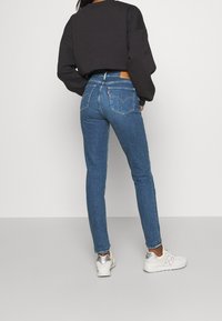 Slim-fit modré džíny s středním pasem, vyznačující se koženou nášivkou vzadu, zadními kapsami a mírným vyblednutím. Spárováno s černým zkráceným svetrem a bílými teniskami.