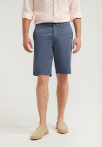 Shorts en coton bleu à coupe droite, arrivant au genou, avec un devant plat et des poches latérales. Associés à des chaussures slip-on beiges.