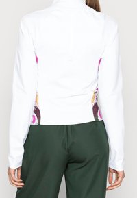 Witte sportieve jas met lange mouwen en hoge kraag. Heeft kleurrijke patronen in roze, oranje en zwart aan de zijkanten. Gladde textuur.