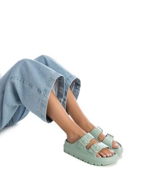 Sandalias verde menta con dos correas ajustables y detalles de hebilla. Suela gruesa con un agarre texturizado. Usadas con pantalones de mezclilla.