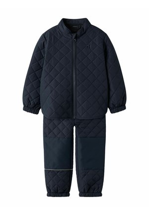 Detská súprava tmavomodrej prešívanej bundy a nohavíc s elastickými manžetami a zosilnenými záplatami na kolenách, bunda má predný zips.