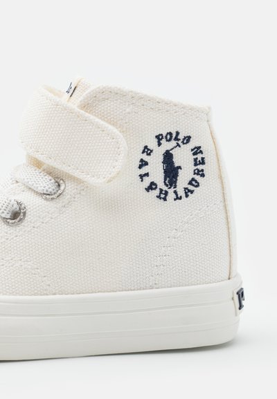 Witte canvas hoge sneakers met een klittenbandsluiting, zilveren ogen en een marineblauw geborduurd logo op de zijkant. Rubberen zool.