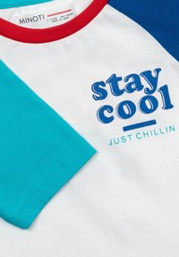 T-maica s kratkimi rokavi z belo podlago, turkiznimi in modrimi rokavi, rdečim ovratnikom ter natisnjenim besedilom "stay cool" in "JUST CHILLIN" v modri barvi.