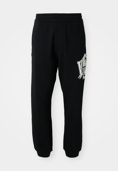 Pantalones de chándal negros hechos de un tejido suave, con una cinturilla y puños acanalados. Incluye un estampado gráfico en blanco y gris en la pierna izquierda.