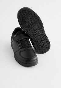 Baskets de sport noires avec une tige en cuir lisse, système de laçage et fermeture Velcro, semelle en caoutchouc texturé avec un motif en nid d'abeille.