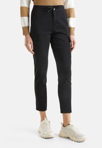 Černé, zkrácené cargo kalhoty s bočními kapsami, zapínáním na knoflík a stahovacími šňůrkami v pase, doplněné bílými sportovními teniskami.