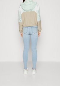 Lekka kurtka w kolorowe bloki w miętowym zielonym, beżowym i białym kolorze. Posiada regulowaną kieszeń, elastyczny pas i luźny krój. W zestawie z jasnoniebieskimi skinny jeansami.