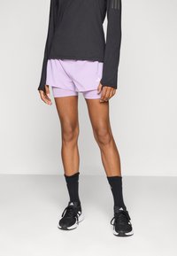 Haut noir à manches longues avec des poignets ajustés, short léger violet, chaussettes de sport noires, et chaussures de course noires avec semelles blanches.