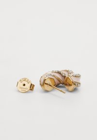 Gold-tone stainless steel earring with twisted design and crystal accents. Features a smooth, light pink curve and visible branding.