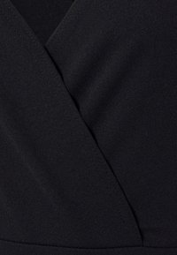 Svart omlotklänning i tyg med en slät textur och v-ringad design. Synliga sömmar längs kanterna. Klassisk, minimalistisk stil.